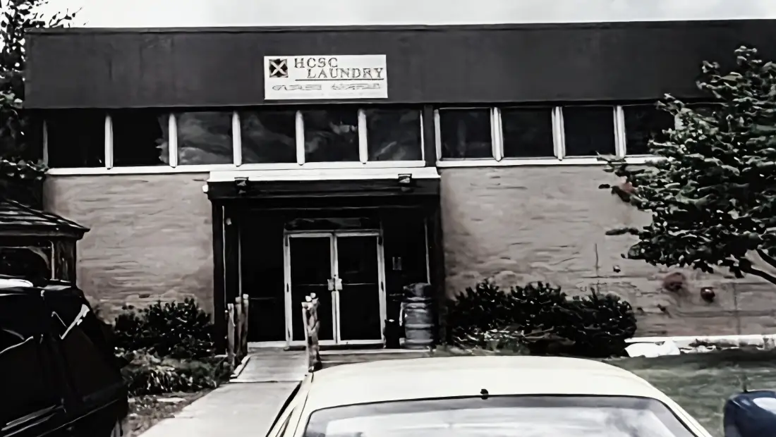 Exterior view of HCSC Laundry storefront with double doors, sign above entrance, and a yellow car parked in front.
